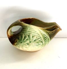 a green and brown vase sitting on top of a white table