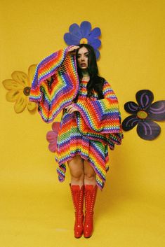 a woman in a colorful dress and red boots is posing for the camera with her hands on her head