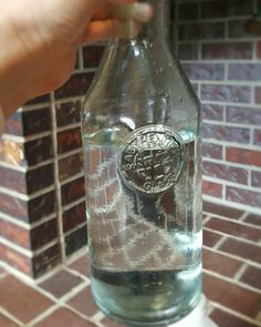 a person is holding a glass bottle with water in it on a table next to a brick wall