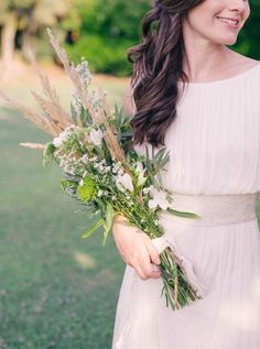 a woman wearing a white dress holding a bouquet of flowers and greenery in her hand