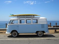 an old vw bus with a surfboard on the roof parked in front of the ocean