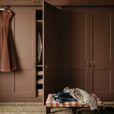 an open closet with clothes hanging on the doors and a bench in front of it