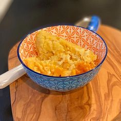 a bowl filled with food sitting on top of a wooden table next to a spoon