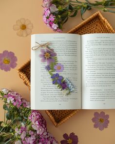 an open book sitting on top of a table next to purple flowers and wicker baskets