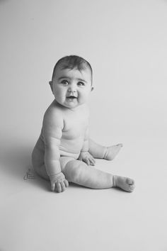 a black and white photo of a baby sitting on the floor looking at the camera