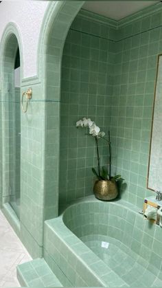 a bath tub sitting next to a bathroom sink under a mirror with flowers in it