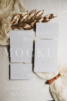 two white cards with gold leaves on them next to a flower and some other items