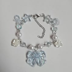 This bracelet is 7 inches long with a 2-inch extender chain, making it adjustable. It features a large iridescent bow charm in the center, surrounded by small star and flower charms. There are also faux pearls and clear faceted beads along the chain. The bracelet is held together by a metal chain and lobster clasp, allowing for a bit of flexibility in the fit. The overall look is light and delicate with a mix of clear and pearl-like elements. Coquette Bracelets, Coquette Bracelet, Bracelet Gift Ideas, Handmade Charm Bracelets, Bracelet Trendy, Chain Making, Bracelet Pearl