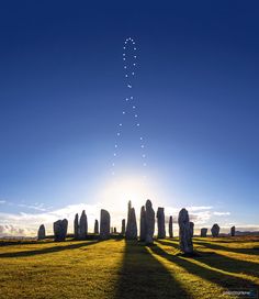 the sun is shining over stonehenge in an open field with grass and blue sky