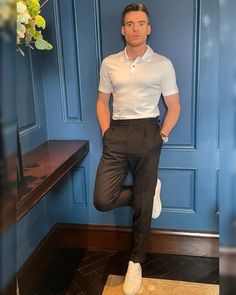 a man standing in front of a blue wall with his feet on the ground wearing white shoes