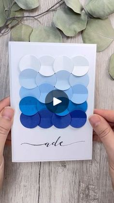 two hands holding up a card with blue and white circles on it, next to eucalyptus leaves