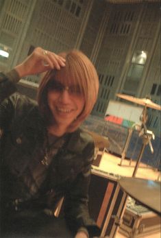 a woman sitting in front of a drum set smiling at the camera with her hand on her head