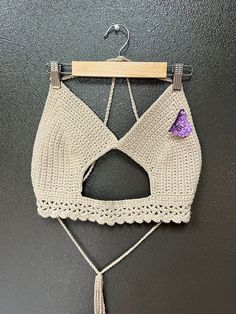 a crochet bralet hanging on a wall with a wooden hanger attached to it