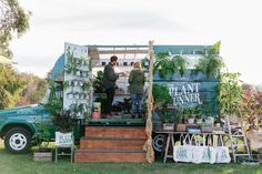 two people standing at the back of a food truck with plants on it's side