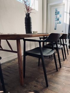 a wooden table with four black chairs and a vase on the wall in front of it