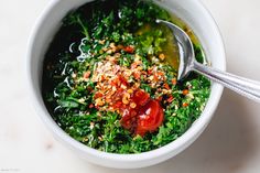 a white bowl filled with greens, tomatoes and other toppings next to a spoon