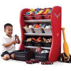 a little boy sitting on the floor next to a toy shelf with toys in it