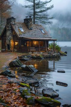 a log cabin sits on the edge of a body of water with rocks in front of it