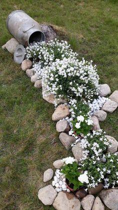 there is a flower bed made out of rocks and an old metal barrel on the grass