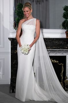 a woman in a white wedding dress standing next to a fireplace with a veil over her head