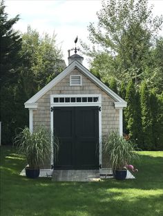 a garage with two plants in front of it and trees around the back yard area