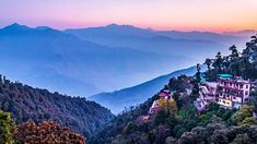 the mountains are covered in lush green trees and houses on top of them, as the sun is setting