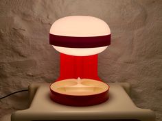 a red and white lamp sitting on top of a table next to a gray wall