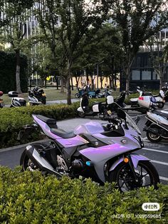 several motorcycles parked in a parking lot next to bushes and trees with buildings in the background