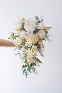 a bridal bouquet being held up by someone's hand with white flowers and greenery