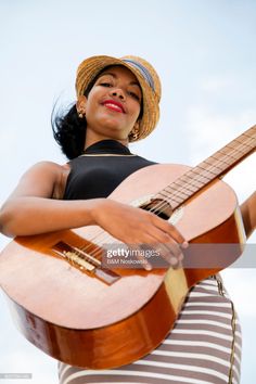 a woman holding an acoustic guitar and wearing a straw hat, against a blue sky