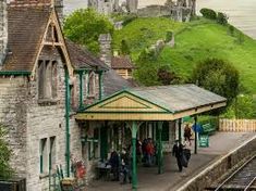 people are standing at the train station in front of a green hill with castle like buildings