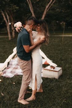 a man and woman standing next to each other in front of a blanket on the grass