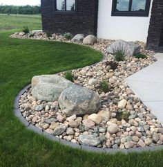 a rock garden in front of a house with grass and rocks on the ground next to it