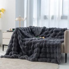 a living room with a couch and chair covered in a gray fluffy blanket on the floor