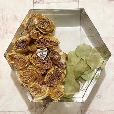 some dried flowers and leaves in a glass box on a marble surface with a heart shaped sticker