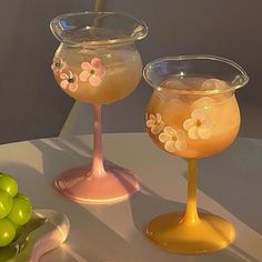 two wine glasses sitting next to each other on a table with grapes in the background