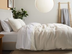 a bed with white linens and pillows in a room next to a potted plant