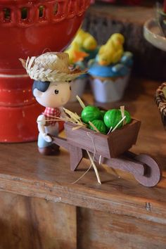 a small toy boy pulling a wheelbarrow filled with green eggs on top of a wooden table