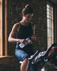 a woman sitting on a stationary exercise bike drinking water