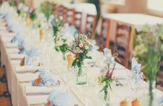 a long table is set with blue and white napkins, vases filled with flowers and greenery