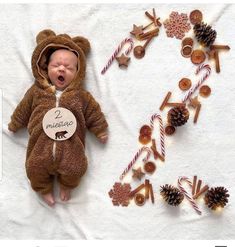 a baby in a bear costume laying next to christmas decorations and candy canes on a white blanket