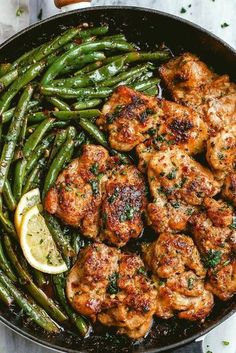 chicken and green beans in a skillet with lemon wedges