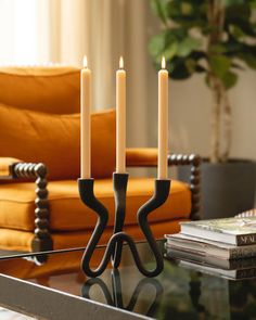 three candles are sitting on a glass table in front of a yellow chair and orange couch