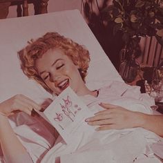 a woman laying in bed holding a card with her mouth open and smiling at the camera