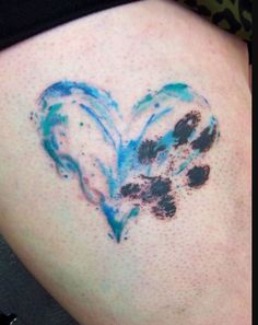 a heart shaped tattoo on the back of a woman's upper arm, with blue ink splatters