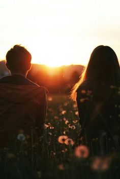 two people are sitting in the grass watching the sun go down behind them with their backs to each other