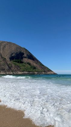 a beach with waves coming in to the shore and a large mountain in the background