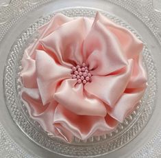 a pink flower is sitting on top of a glass cake plate with beaded trim