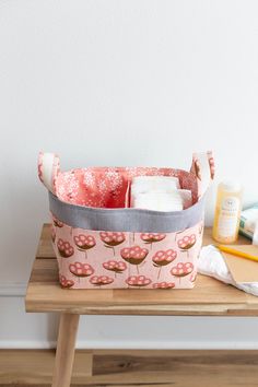 a pink flowered fabric storage basket on top of a wooden table next to a white wall