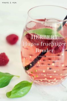 a wine glass filled with raspberries on top of a white table next to green leaves